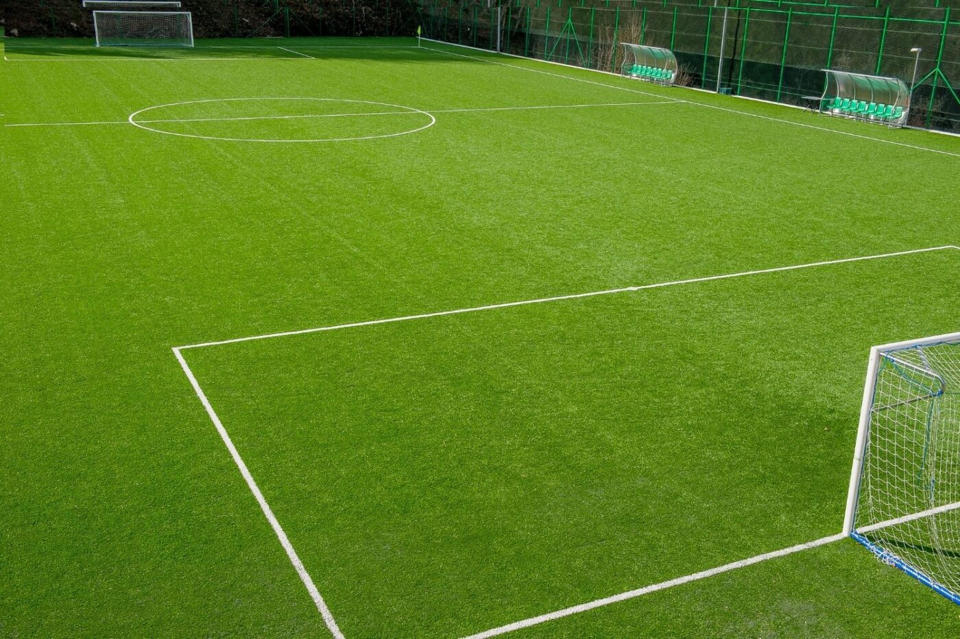 An empty, well-maintained soccer field featuring lush turf from a Top-Rated Artificial Grass Installer Phoenix, with crisp white boundary lines, two goals, and benches along the sideline. No players are present on the field.