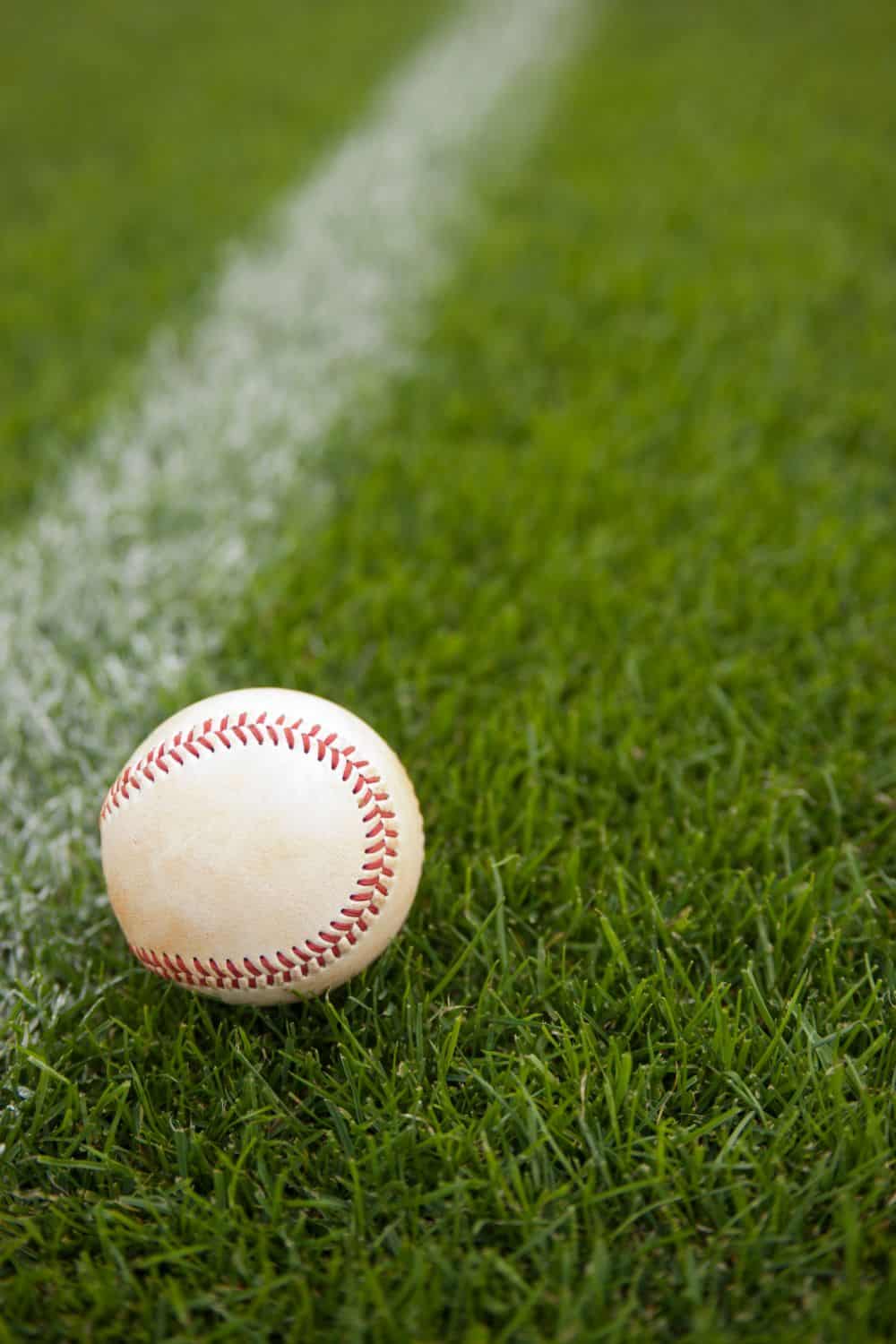 A baseball resting on green grass near a white chalk line highlights the work of a Top-Rated Artificial Grass Installer Phoenix, showcasing realistic turf perfect for any field.