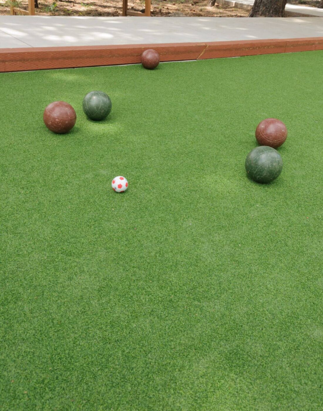 A bocce ball court with four large colored bocce balls and a small white and red pallino ball scattered on green turf, expertly installed by a Top-Rated Artificial Grass Installer Phoenix. A wooden border runs along the back edge of the court.