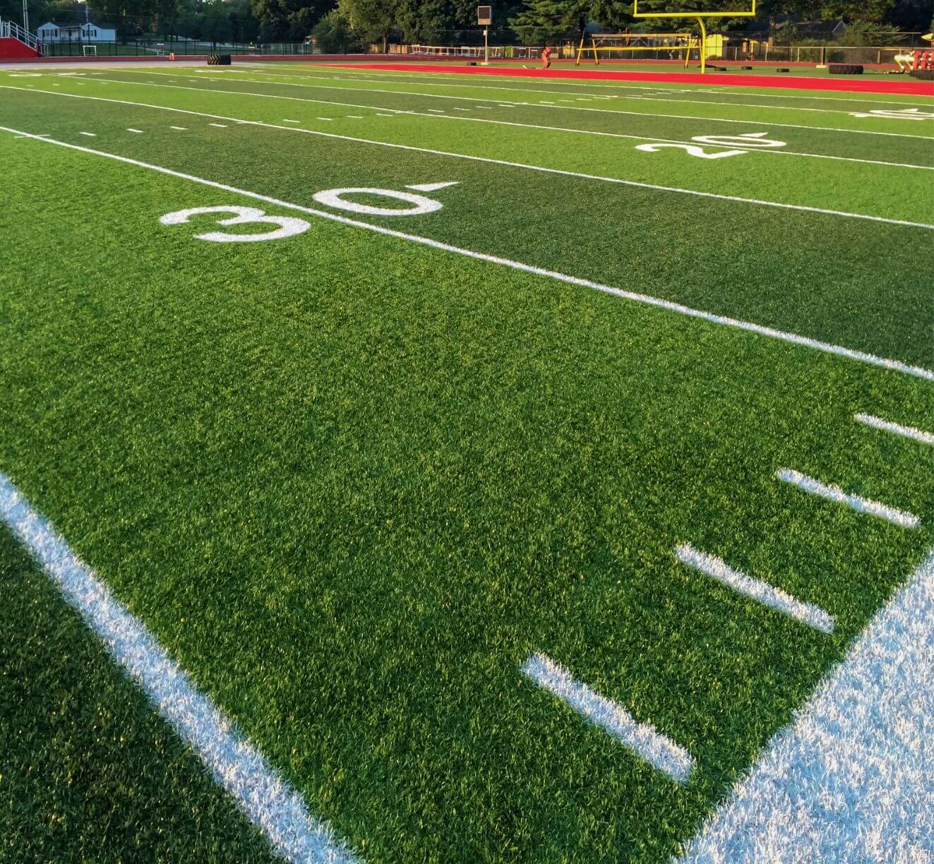 A close-up view of a football field shows the 30-yard line, white yard markers, and vibrant green turf installed by a Top-Rated Artificial Grass Installer Phoenix, with yellow goalposts shining in the sunlight.